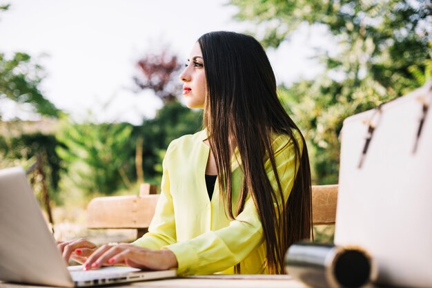 Powabna brunetka pozuje z laptopem w parku