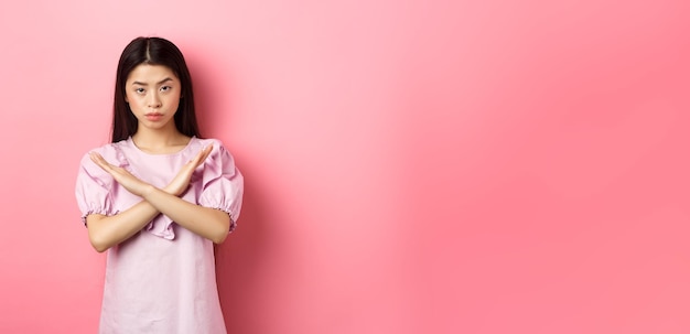 Bezpłatne zdjęcie poważna chińska dziewczyna pokazuje znak krzyża, wykonuj gest zatrzymania i wyglądaj na pewną osobę z bloku, która mówi „nie” i „ponownie”.