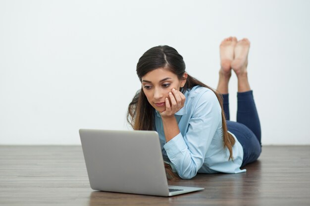 Poważna kobieta leżącego na podłodze i pracy na laptopie