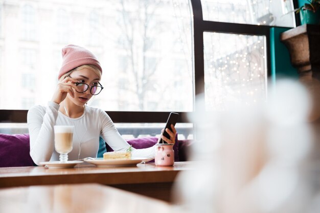 Poważna młoda kobieta je telefon komórkowego w kawiarni i używa