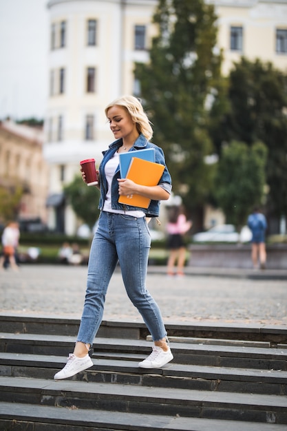 Poważna Modelka Blondynka Idzie Na Zajęcia Robocze Przez Centrum Miasta, Trzymając W Rękach Komputer Z Notebookami Do Kawy Rano