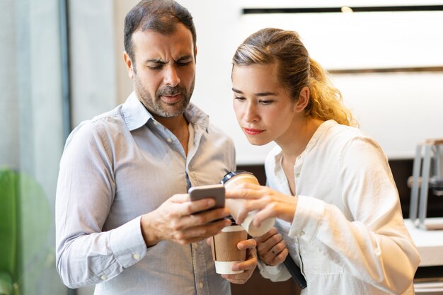 Poważni męscy i żeńscy koledzy czyta wiadomość na telefonie komórkowym