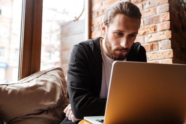 Poważny Brodaty mężczyzna używa laptop w kawiarni