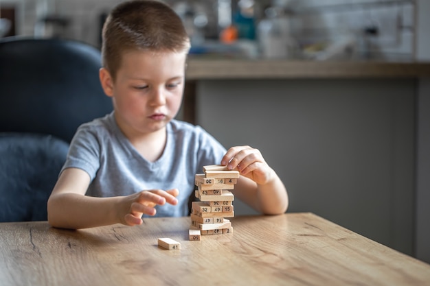 Poważny mały chłopiec gra w grę planszową z drewnianą wieżyczką.
