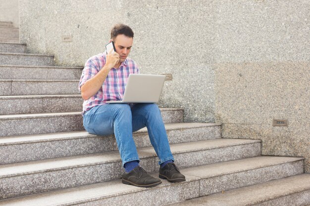 Poważny mężczyzna używa telefon komórkowego i sprawdza kartotekę na laptopie