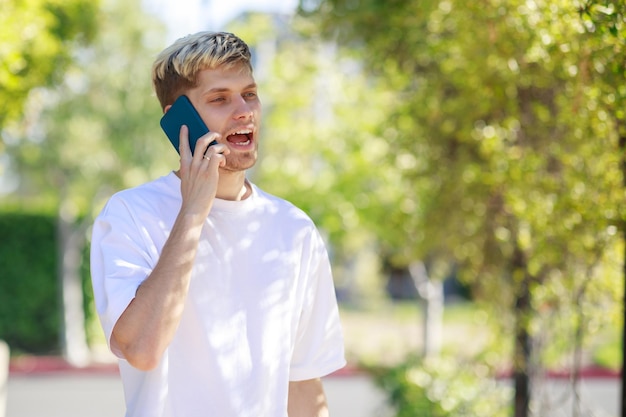 Poważny młody człowiek stojący w parku i rozmawiający przez telefon