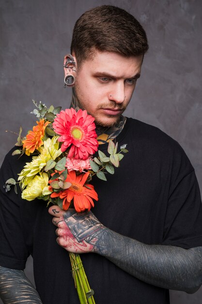 Poważny młody człowiek z przebitym nosem i uszami trzyma bukiet kwiatów w ręku