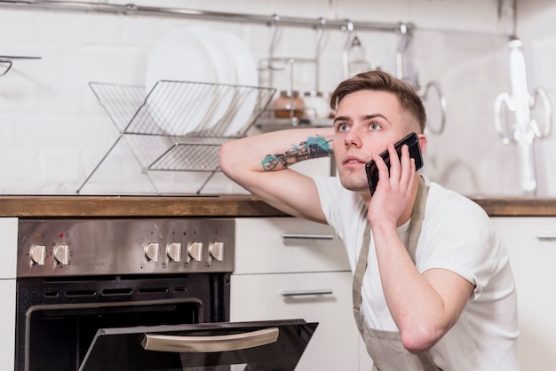 Poważny młody męski jest ubranym fartuch opowiada na telefonie komórkowym patrzeje daleko od