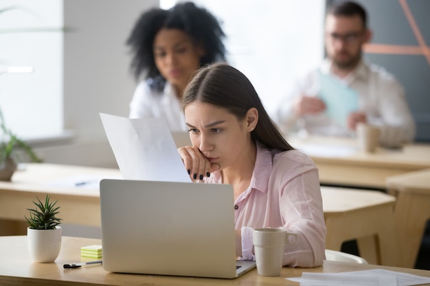 Poważny pracownik uważnie czytający dokument skupiony na myśleniu w coworkingu