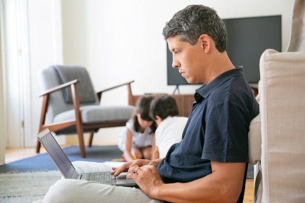 Poważny profesjonalista pracujący w domu, siedząc na podłodze i używając laptopa