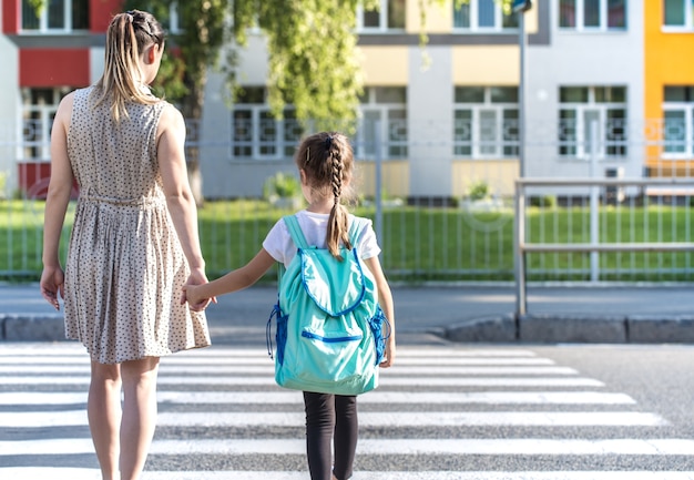 Powrót do koncepcji edukacji szkolnej z dziećmi dziewczynki, uczniów szkół podstawowych, niosąc plecaki idąc do klasy trzymając się za rękę razem spacerując