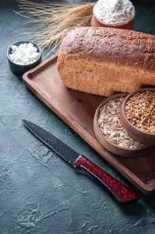 Powyżej widok czarnego chleba kromki mąki w misce na desce i kolce na noże surowa pszenica owsianka po lewej stronie na mieszanych kolorach w trudnej sytuacji
