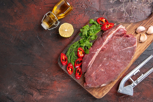 Bezpłatne zdjęcie powyżej widok czerwonego mięsa na drewnianej desce do krojenia i czosnku posiekanego zielonego pieprzu opadłej butelki oleju z cytryną na ciemnym tle