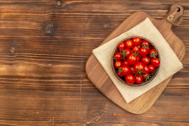 Powyżej widok świeżych pomidorów na brązowej misce na desce do krojenia na drewnianej desce z wolną przestrzenią