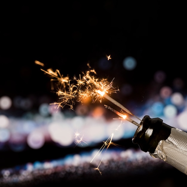 Bezpłatne zdjęcie pożarniczy sparkler w szampańskiej butelce na bokeh tle przy nocą