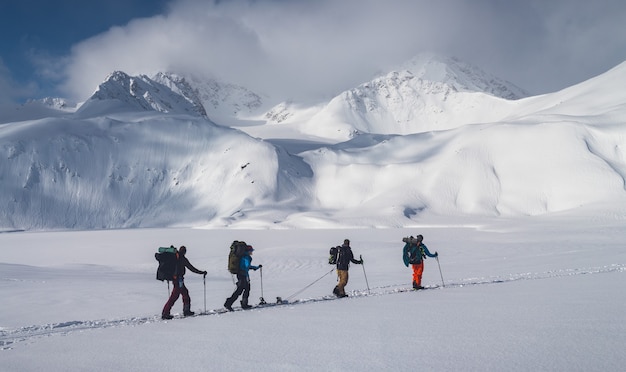 Poziome ujęcie grupy ludzi wędrujących po górach pokrytych śniegiem pod zachmurzonym niebem