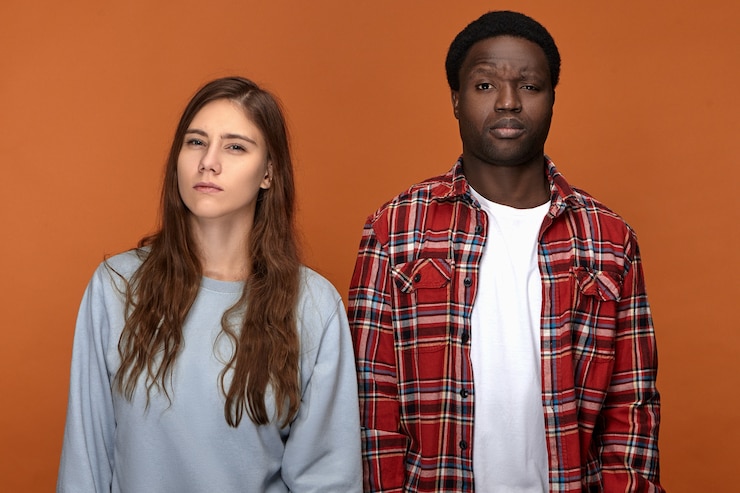 Bezpłatny plik Zdjęcie poziome ujęcie młodej kobiety rasy kaukaskiej i mężczyzny afro american stojących obok siebie w zwężone oczy, z podejrzanymi wyrazami twarzy. emocje i reakcja