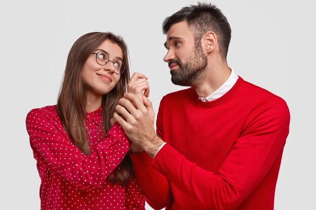 Poziome ujęcie zadowolonej kobiety patrzy na męża, który ma błagalny wyraz i trzyma ją za rękę, nosi czerwone ubranie, ma przyjemną rozmowę, odizolowane na białym tle. Ludzie