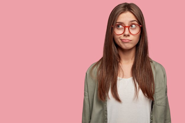 Poziomy portret przemyślanego studenta pozuje na różowej ścianie