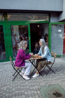 Pozytywna dojrzała kobieta i siwowłosy azjatycki towarzysz z kawą na tarasie kawiarni na świeżym powietrzu