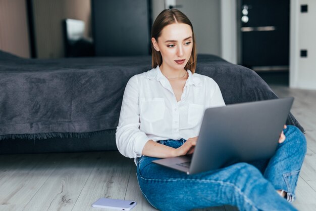 Pozytywna kobieta korzystająca z laptopa w domu, siedząca na podłodze