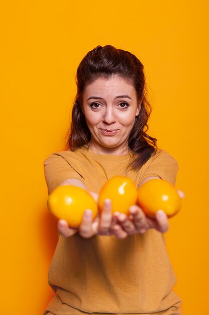 Pozytywna kobieta trzymająca żółte owoce cytrusowe w studio