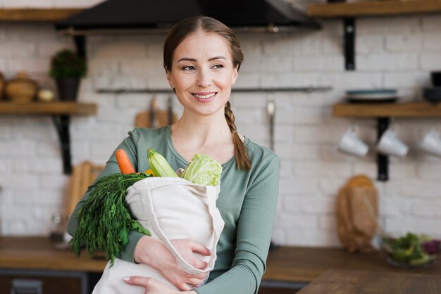 Pozytywna młodej kobiety mienia torba z organicznie warzywami