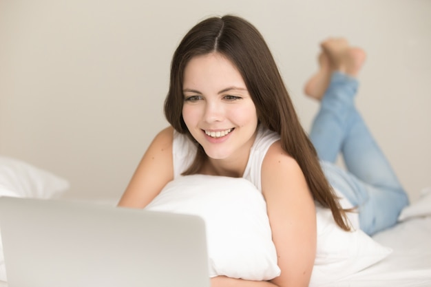 Pozytywna nastoletnia dziewczyna robi zakupy online w łóżku w domu