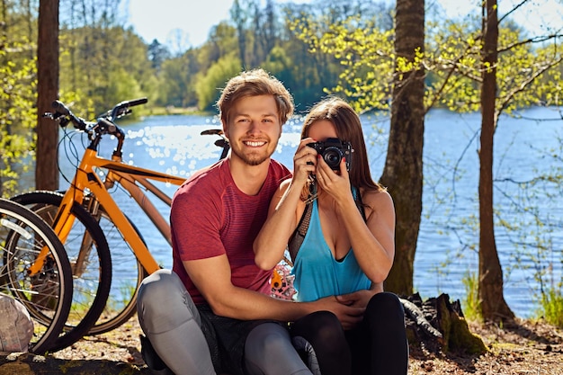 Pozytywna para sportowy relaks w pobliżu rzeki po przejażdżce rowerowej. Kobieta robienia zdjęć na kompaktowym cyfrowym aparacie fotograficznym.