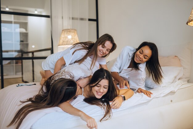 Pozytywne młode dziewczyny koleżanki kobiet w pomieszczeniu na łóżku na imprezie panieńskiej w domu