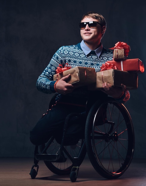 Bezpłatne zdjęcie pozytywny człowiek na wózku inwalidzkim z prezentami na ciemnoszarym tle.