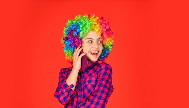 Pozytywny i wesoły. szczęście z dzieciństwa. dzieciak wygląda śmiesznie we włosach tęczowej peruki. farbowanie włosów u fryzjera. dziecko zabawy. z okazji urodzin. mała dziewczynka kolorowa peruka mówić na telefon.