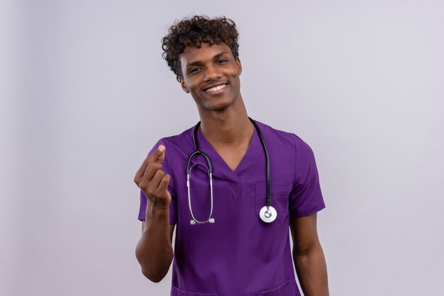 Pozytywny młody przystojny ciemnoskóry lekarz z kręconymi włosami w fioletowym mundurze ze stetoskopem uśmiechnięty i