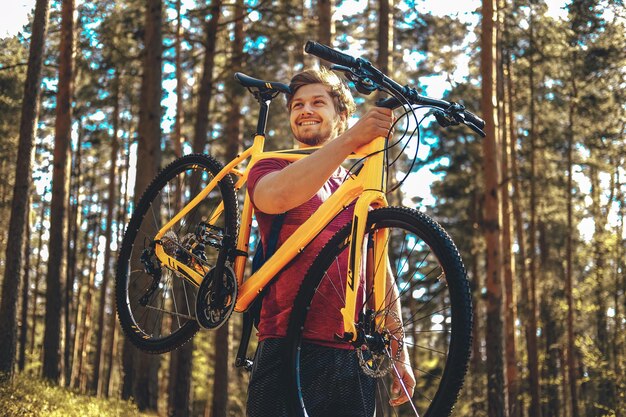 Pozytywny sportowy mężczyzna trzymający żółty rower górski nad głową.