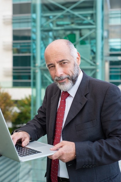 Pozytywny ufny szary z włosami biznesmen używa laptop