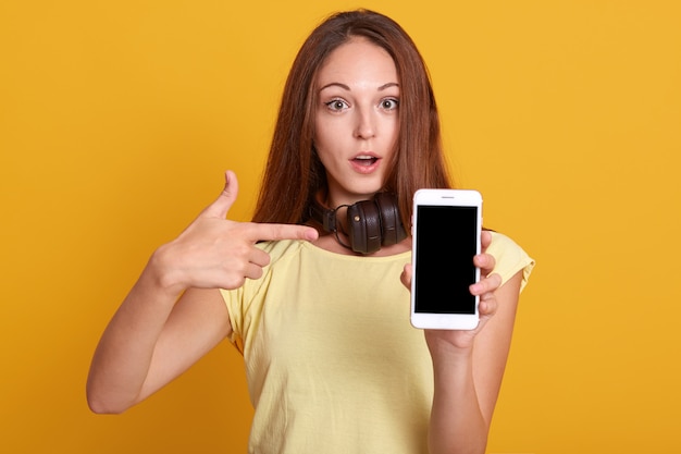 Pracowniany sho urocza kobieta pokazuje telefon z pustym ekranem i wskazuje na nim jej palcem wskazującym