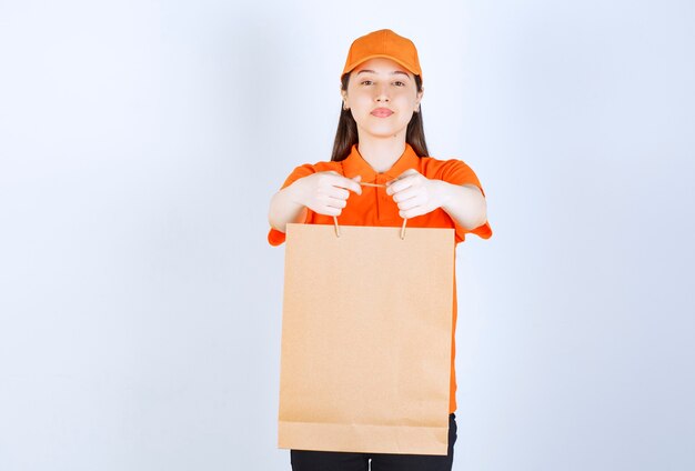 Pracownica usługowa w pomarańczowym mundurze trzymająca torbę na zakupy i prezentująca ją klientowi.