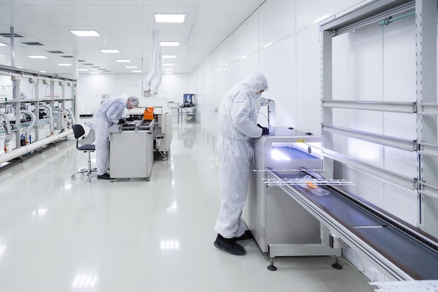 Pracownicy fabryki w białych garniturach laboratoryjnych i czarnych lateksowych rękawiczkach, pracujący z nowoczesnym sprzętem w bardzo czystym pomieszczeniu