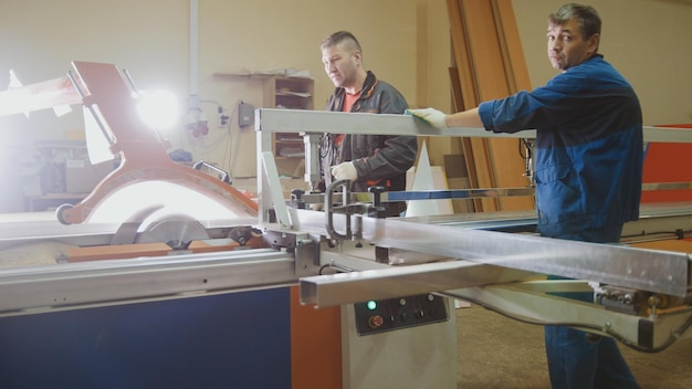 Pracownicy stolarze tną deskę drewnianą na piły elektrycznej w fabryce mebli, szeroki widok