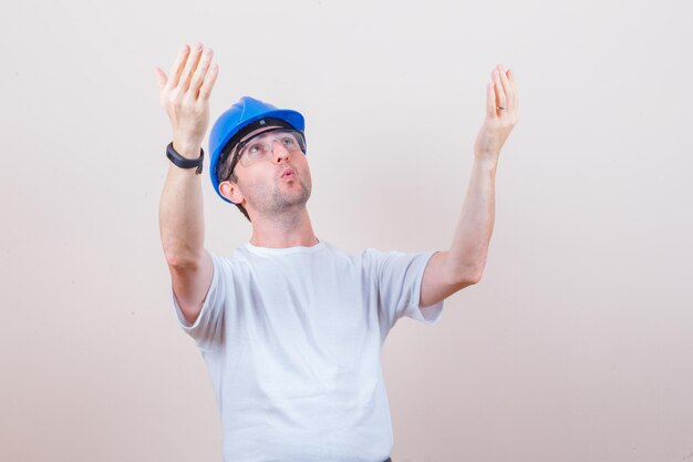 Pracownik budowlany podnoszący ręce, patrząc w koszulkę, kask i wyglądając na zaskoczonego