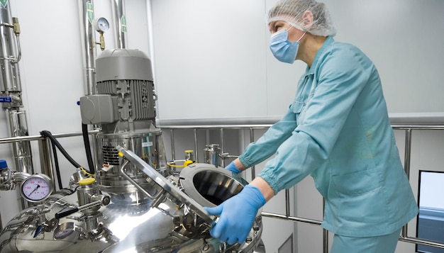 Pracownik fabryki farmaceutycznej w odzieży ochronnej obsługującej linię produkcyjną w sterylnym środowisku