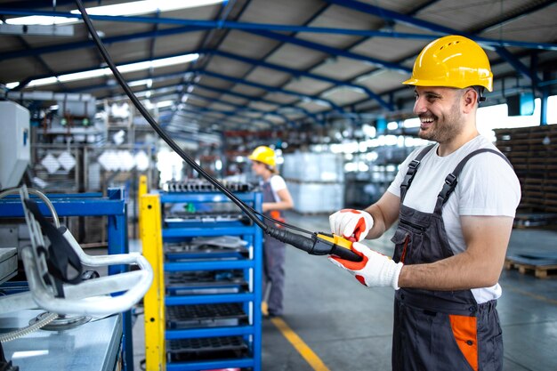 Pracownik fabryki ubrany w mundur i kask obsługujący maszynę przemysłową z joystickiem z przyciskiem w hali produkcyjnej