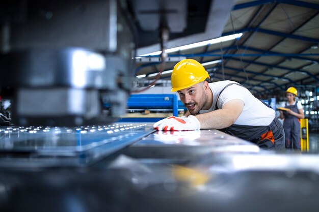 Pracownik fabryki w mundurze ochronnym i kasku obsługującym maszynę przemysłową na linii produkcyjnej