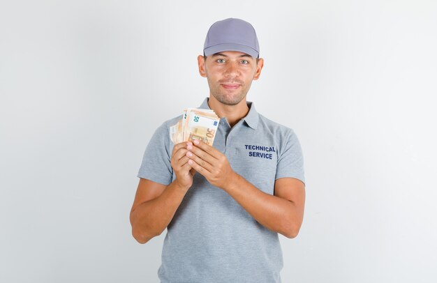 Pracownik obsługi technicznej w szarym t-shircie z czapką z banknotami euro