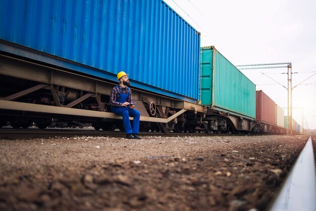 Pracownik płci męskiej sprawdzający przyczepy kolejowe z kontenerami transportowymi przed wyjazdem