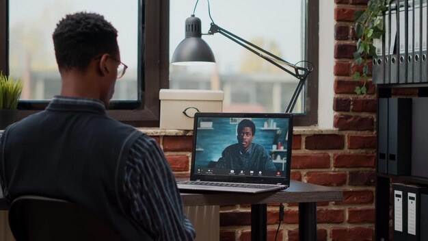 Pracownik startowy korzystający ze zdalnej rozmowy wideo na laptopie, aby porozmawiać z kolegą w pracy. Mężczyzna uczestniczy w spotkaniu biznesowym z osobą na wideokonferencji online dla telekomunikacji i telepracy.