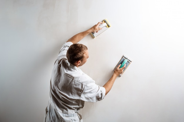 Bezpłatne zdjęcie pracownik szlifowanie białej ściany papierem ściernym.