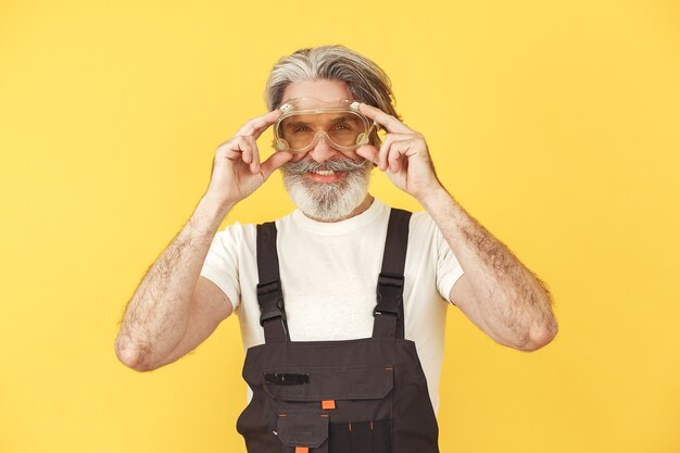 Pracownik w kombinezonie. Człowiek z narzędziami. Senior w żółtych okularach.