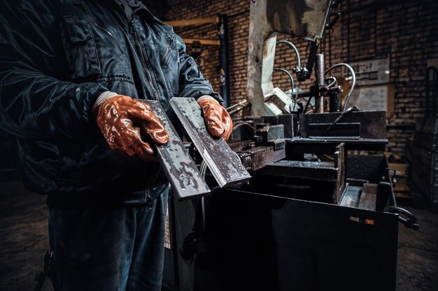 Pracownik w rękawicach ochronnych trzyma świeżo ścięty kawałek metalu.