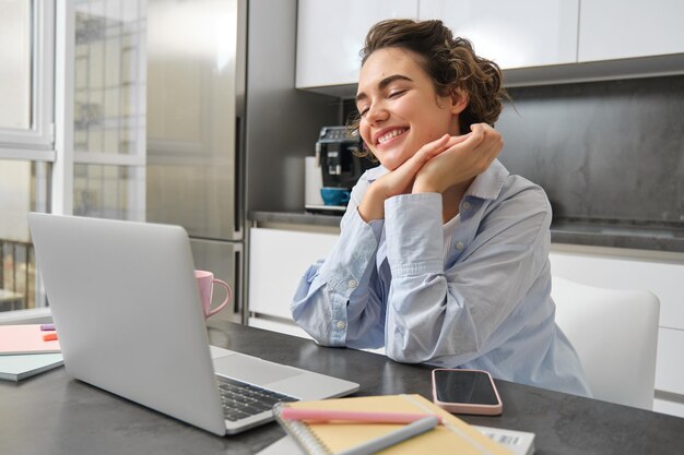 Pracująca kobieta korzystająca z laptopa w domu, wykonująca formalności związane z podatkami, oglądająca kurs online w kuchni